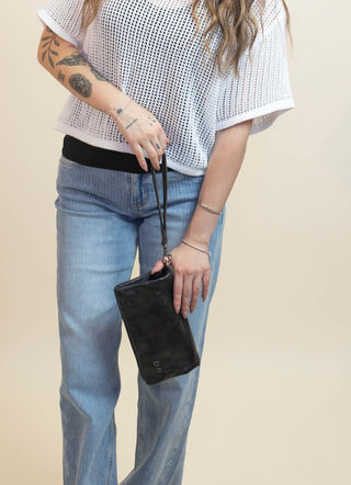 A woman modeling a white short-sleeve knit top with a black underlayer, paired with light blue jeans and holding a black clutch bag, set against a plain beige studio background.
