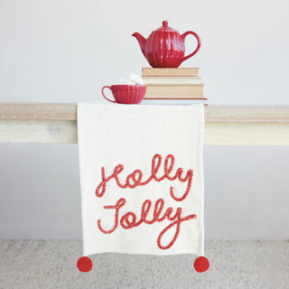 Close-up of red Holly Jolly script embroidery and pom-pom on runner