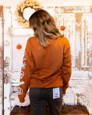 Styled view of Rust-colored Halloween sweatshirt with spooky seasonal emblems and sleeve print